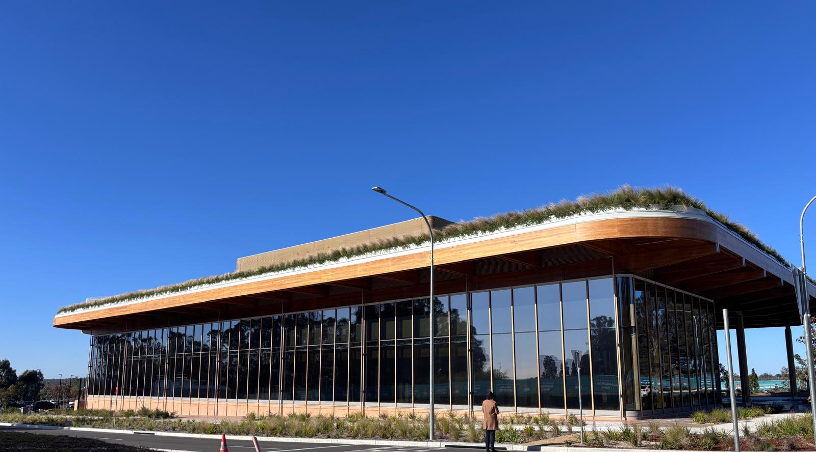 A completed public building with a broad overhanging engineered timber roof and full-height glazing